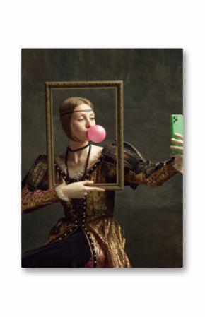 Portrait of pretty young girl, princess with bubble gum, holding picture frame and taking selfie with phone against dark green background. Concept of history, renaissance art, comparison of eras