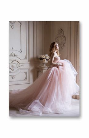 Beautiful young blond woman in luxurious long pink dress posing in vintage room interior. indoor studio shot.