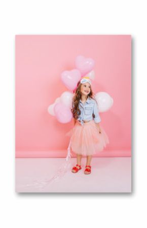 Lovely happy moments of little amazing girl with long brunette hair having fun with balloons isolated on pink background. Wearing tulle skirt, princess cute mask on head, expressing true emotions