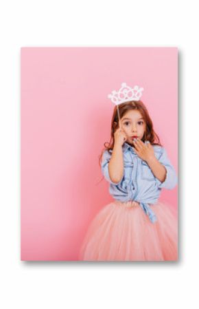 Surprised pretty young girl in tulle skirt with crown on head expressing isolated on pink background. Amazing cute little princess at carnival. Place for text