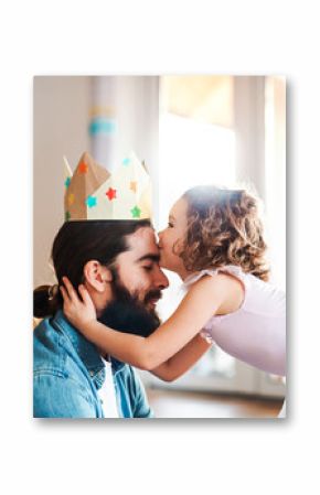 A side view of small girl with a princess crown and young father at home, playing.