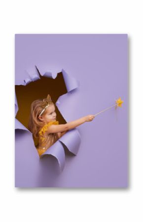 Cute little child girl in princess costume breaks through a colored purple paper wall. Points with a magic wand to the empty space on the right. Toddler funny emotions face.