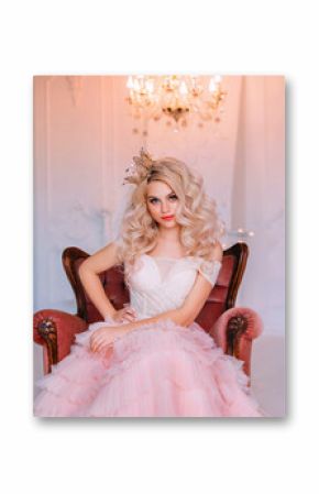 Charming beautiful delightful young girl princess sitting in antique vintage armchair waiting fairy miracle. Queen woman smiles mysteriously cute. Blonde long curly hair. Delicate pink airy sexy dress