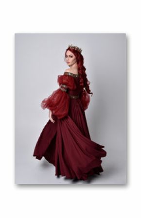 Portrait of a beautiful woman with red hair wearing  a  flowing Burgundy fantasy gown and golden crown.  full length standing pose, isolated against a studio background 