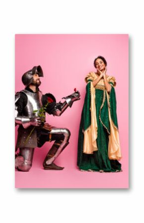Romantic knight kneeling before princess in elegant medieval costumes on pink background