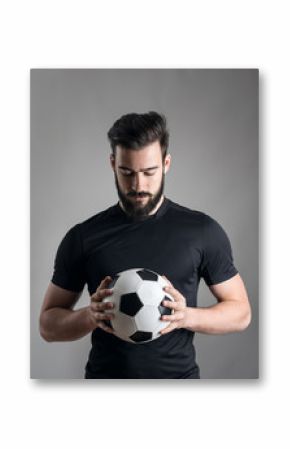 Intense portrait of football player holding and looking at the ball focused over gray studio background. Determination concept.