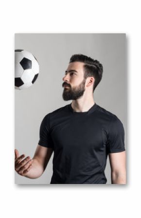 Side view of bearded young football or soccer player throwing ball over gray studio background.