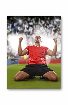 happy and excited football player in red jersey celebrating scoring goal kneeling on grass pitch