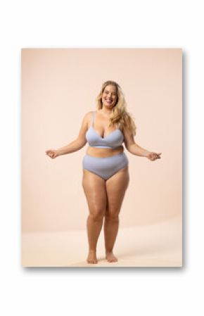 Plus size model in blue underwear smiles on beige background, copy space