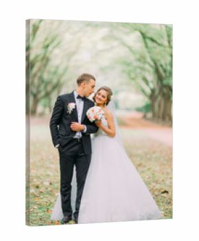 Full portrait of happy young wedding couple standing arm-in-arm in park