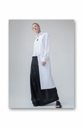 Stylish girl with blond short haircut in minimalist clothes. White linen long shirt and black long linen skirt.