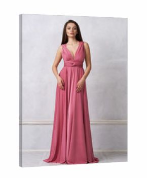 Beautiful long haired young woman dressed in stylish red bandeau maxi dress posing against white wall on background. Elegant brunette female model demonstrating evening outfit in studio.