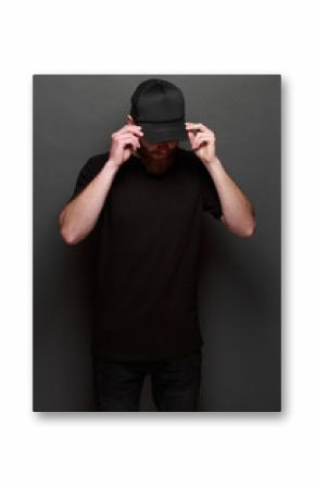 Hipster handsome male model with beard wearing black blank t-shirt and a black baseball cap with space for your logo or design in casual urban style