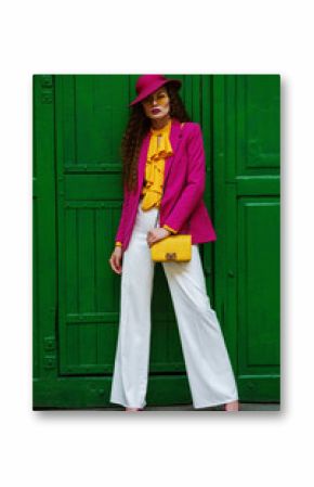 Outdoor full body portrait of young beautiful fashionable woman wearing trendy, colorful clothes, stylish accessories, posing near the green door. Female fashion concept