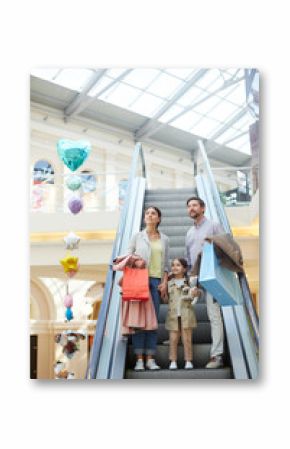 Parents with little girl carrying bags and moving on escalator in light big shopping center enjoying time together