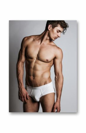 Male model with perfect body in white underwear posing over grey background. Close-up. Studio shot.