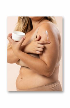 Young Caucasian plus-size model applies cream to her arm on beige background