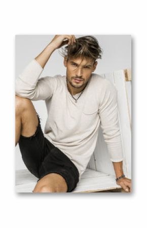 Portrait of handsome man with hand in his hair and sitting on pa