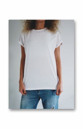 An attractive young woman dressed in a white blank t-shirt and blue jeans posing on a background of a white wall. Vertical mock up. empty space for you logo or design