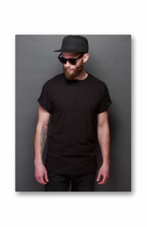 Hipster handsome male model with beard wearing black blank t-shirt with space for your logo or design over gray background