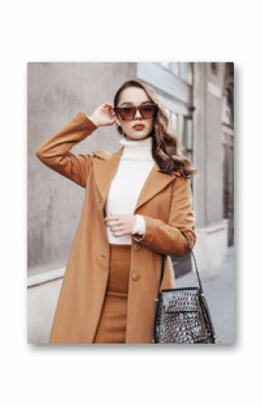 Outdoor portrait of young beautiful fashionable woman wearing trendy leopard print sunglasses, autumn coat, turtleneck, skirt, holding stylish handbag, posing in street of european city