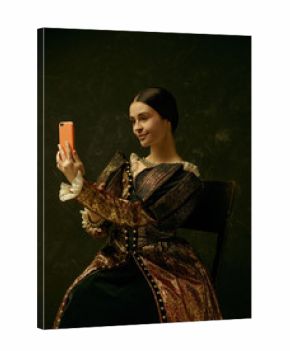 Portrait of a girl wearing a princess or countess dress with mobile phone over dark studio making selfie photo