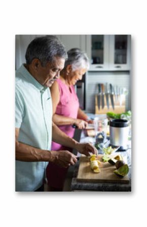 Biracial senior couple cutting fruits into slices on counter while preparing smoothie in kitchen