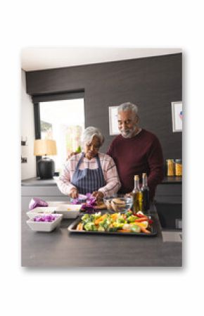 Happy senior biracial couple preparing vegetables and embracing in kitchen at home, copy space