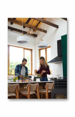 Midsection of caucasian couple preparing salad and vegetables, using tablet in kitchen, copy space