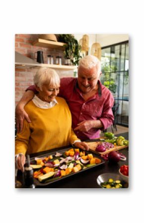 Happy caucasian senior couple preparing fresh vegetables, embracing and talking in kitchen