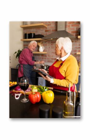 Happy caucasian senior couple preparing vegetables and using tablet in kitchen, copy space