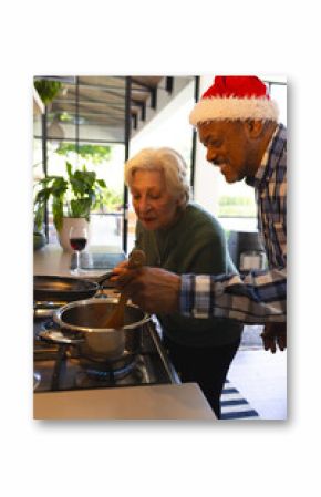 Happy diverse friends couple in santa hat preparing food in sunny kitchen at home