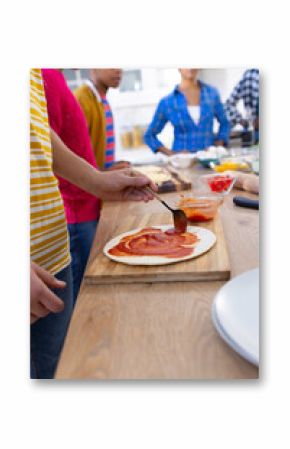 Happy diverse group of teenage friends cooking and making pizza in kitchen