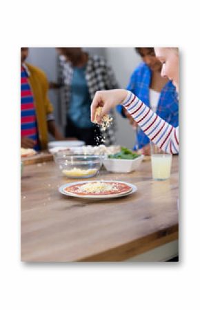 Happy diverse group of teenage friends cooking and making pizza in kitchen