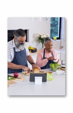 Preparing meal, senior couple chopping vegetables and using tablet in kitchen