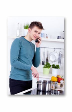 young man cooking a meal and talking on the phone in the kitchen
