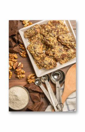 Overhead view of homemade chocolate walnut cookies with ingredients and kitchen utensils on a dark rustic wood table.