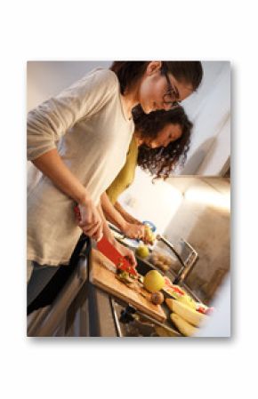 Young female friends in kitchen preparing together vegetarian meal.Preparing fruit salad.Evening.