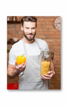 Portrait of a healthy man holding yellow pepper and jar with pasta on the kitchen