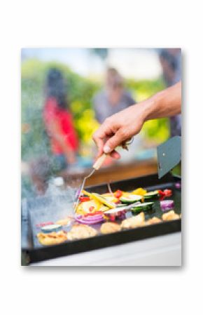 Close-up on hands grilling meat and vegetables on a plancha.