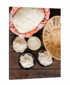 Homemade dough, sourdough in a jar, mix of flours, bread and basket for proof and spatula on a wooden background. Baking concept.