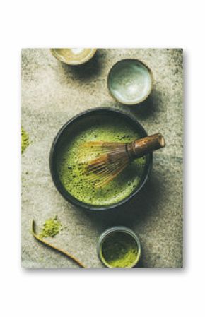 Flat-lay of Japanese tools for brewing matcha tea. Matcha powder in tin can, Chashaku spoon, Chasen bamboo whisk, Chawan bowl and cups for ceremony over concrete background, top view