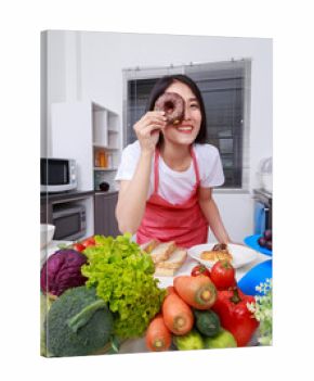 Cheerful woman is covering her eye with chocolated donut in kitchen room