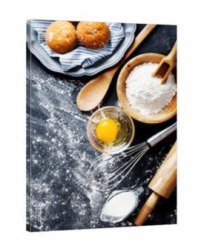 Baking ingredients. Bowl, eggs, flour, eggbeater, rolling pin and eggshells on black chalkboard from above.