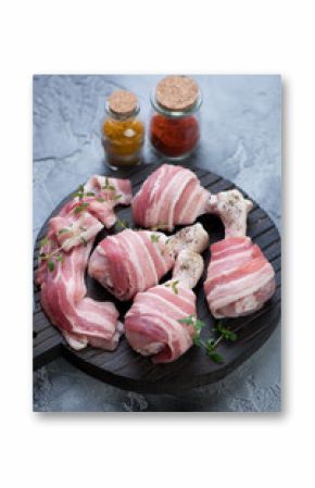 Raw fresh chicken drumsticks wrapped with bacon ready to be cooked, selective focus, vertical shot