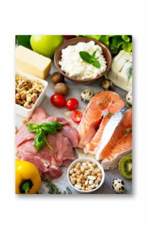 Assortment of a healthy protein source, superfoods on a gray stone background. Meat turkey, salmon, quail eggs, dairy products feta cheese and cottage cheese, beans, spinach, chickpeas, fruit.