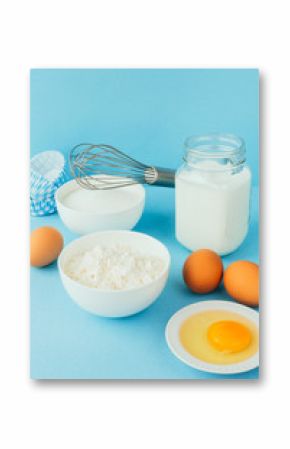 Eggs of chicken, flour in a bowl, sugar, milk in a glass jar whisk ingredient for cooking a bake on a blue background with copy space