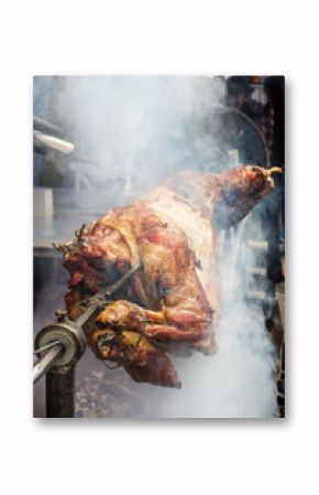 Cook's hand with a knife checks the readiness of the lamb on a spit in the smoke over hot coals. Outdoor grill