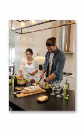 Couple preparing fresh salad and bread in modern kitchen, enjoying cooking together