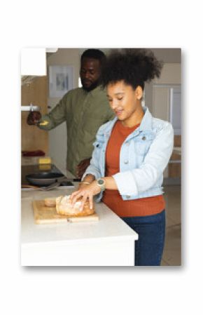 Couple in kitchen preparing meal together, slicing bread and cooking on stove